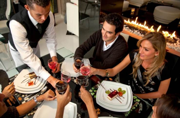 cameriere che serve ad un tavolo del ristorante e persone sedute che brindano