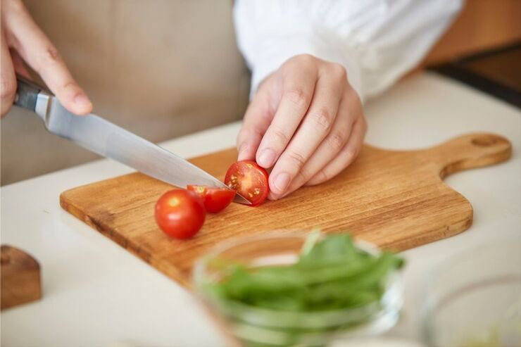 Mano taglia pomodori con coltello su tagliere di legno